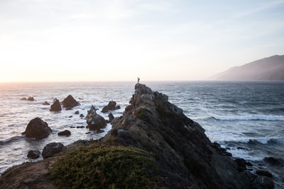人站在岩石悬崖附近的水域
